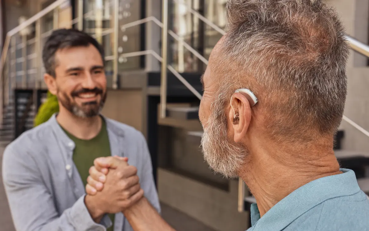 Dois homens se cumprimentando, um deles usando aparelho auditivo