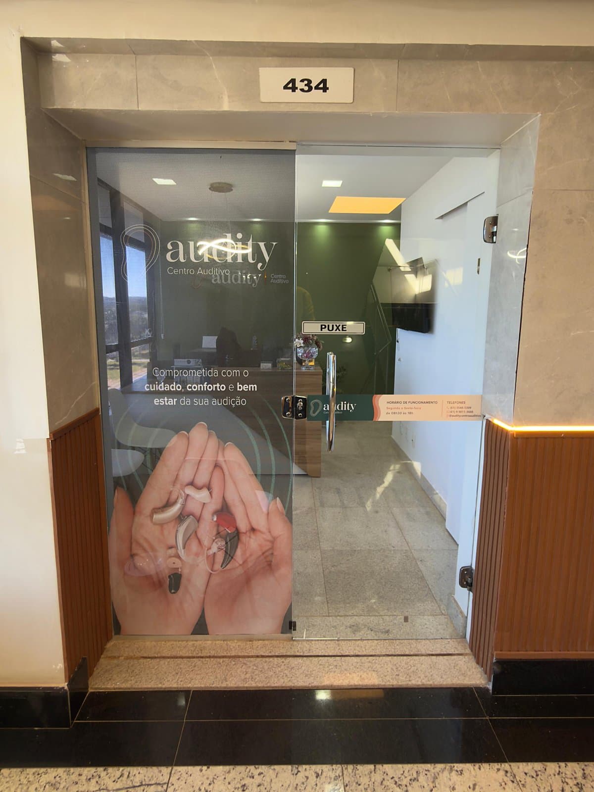 Porta de vidro da sala 434 com a marca Audity e a recepção ao fundo