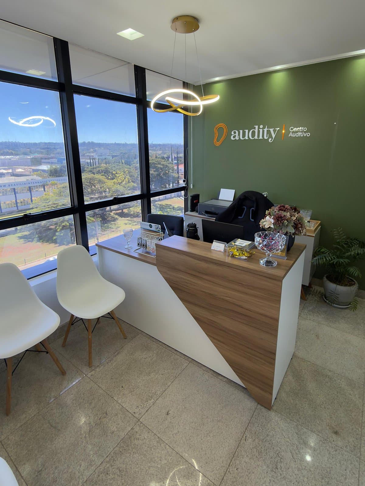 Recepção da Audity com parede verde e logo, balcão de madeira e janelas com vista